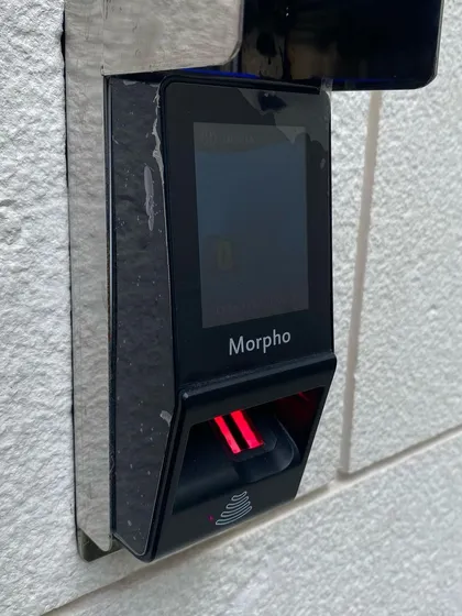 A close-up view of a Morpho biometric reader installed on an exterior wall. The device's robust construction and advanced sensor technology ensure reliable performance for secure, keyless entry in any weather condition.