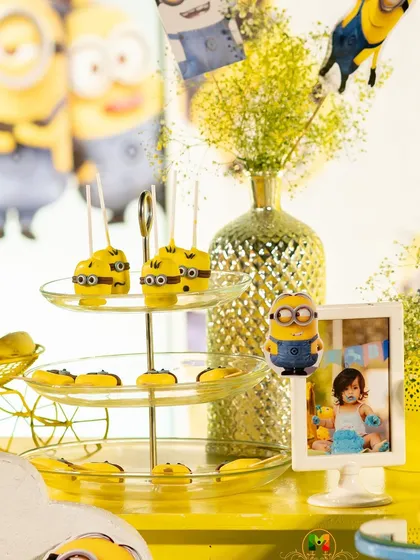 Themed desserts are a must. These Minion-themed cake pops and treats are arranged on a tiered stand, adding to the visual appeal of the dessert table.