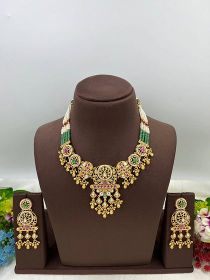 A beautiful antique gold necklace with intricate jaali work and multi-color stones, strung with green and white beads.