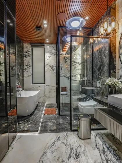 A luxurious bathroom design featuring a freestanding bathtub, a glass-enclosed shower, and walls clad in dramatic black and white marble. The wood-paneled ceiling adds warmth to the space.