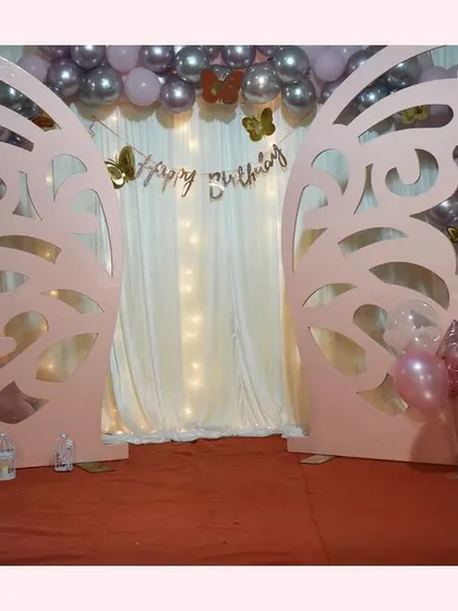 Our giant butterfly wing prop serves as the centerpiece for this enchanting birthday backdrop. Paired with a 'Happy Birthday' banner, fairy lights, and balloons, it creates a magical photo booth for the special day.