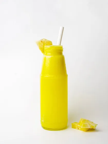 A vibrant yellow pineapple or mango juice in a bottle, presented simply for a clean menu shot.