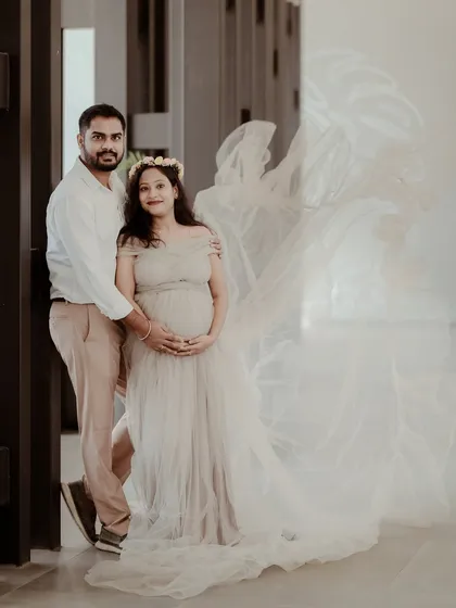 An elegant maternity photoshoot featuring an expecting couple. The mother-to-be wears a beautiful flowing gown, creating a dreamy and artistic portrait that celebrates her pregnancy.
