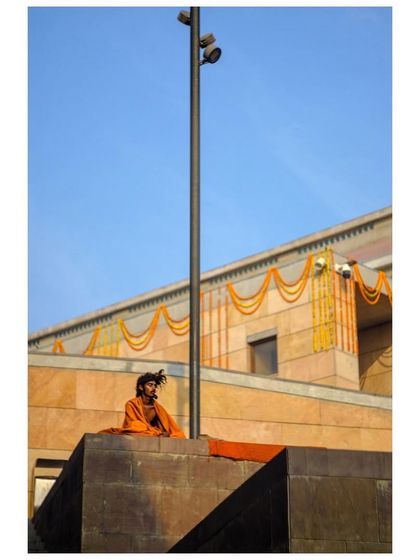 A sadhu in orange robes sits atop the modern architecture of the Kashi Vishwanath temple complex in Varanasi.