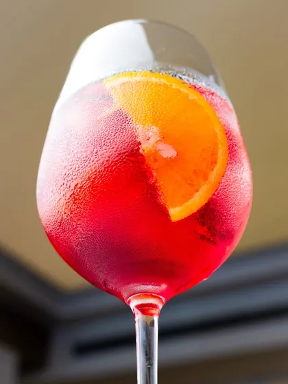 A close-up of a bright red Aperol Spritz. The condensation on the glass and the vibrant orange slice make it look like the ultimate refreshing summer drink.