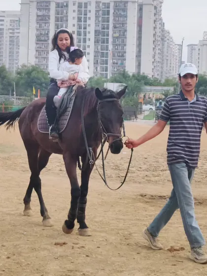 Safety is paramount, especially with our youngest riders. A trainer carefully leads the horse while a mother and child enjoy a ride together in our arena.