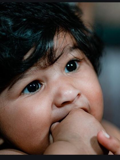 A beautiful close-up shot capturing a baby's innocent expression and big, curious eyes as they chew on their tiny foot.