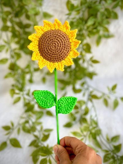 Holding up a single crochet sunflower to show its delicate stem and leaves. It’s perfect for placing in a small vase.