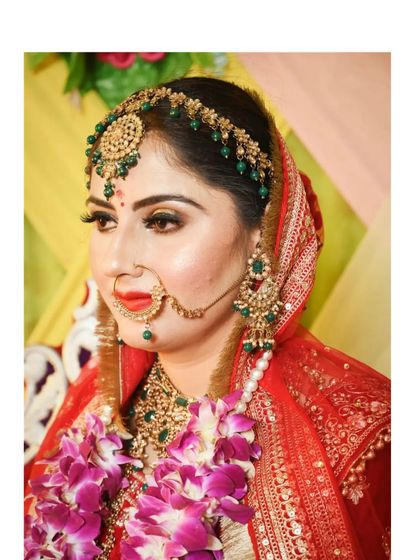 A close-up of a bride's makeup and jewellery. The look features a classic red lip, a beautiful green and gold jewellery set, and a traditional nath.