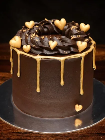 Simple, elegant, and delicious. This dark chocolate truffle cake is finished with a rich ganache, a gold drip, and delicate golden hearts, making it a perfect cake for a first wedding anniversary or any romantic celebration.