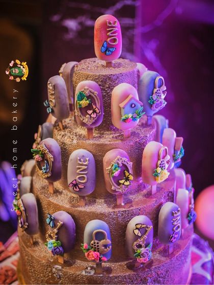 A stunning tower of enchanted-themed cakesicles for a first birthday. Each one is decorated with edible butterflies, flowers, and tiny golden frames, creating a magical and elegant display.