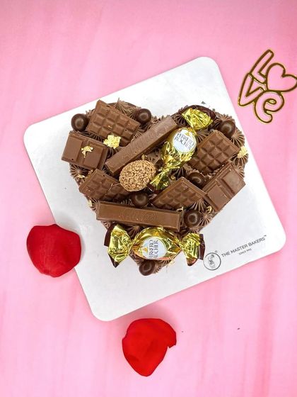 A heart-shaped cake that's a chocolate lover's dream. It's covered in various chocolate bars and Ferrero Rocher, making it a rich and indulgent treat for Chocolate Day or Valentine's.