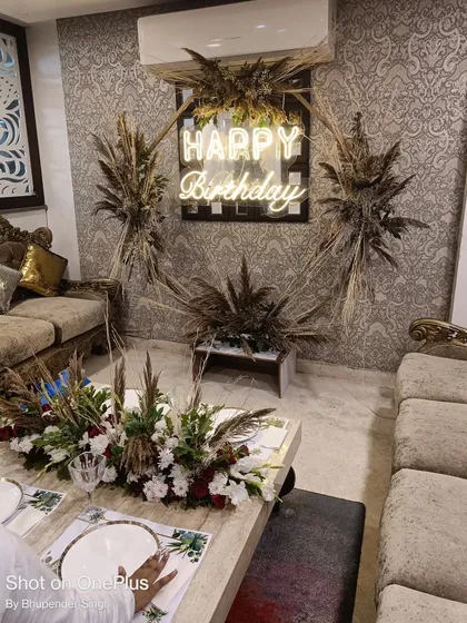 I designed this modern birthday party decor for a client's home. The setup features a trendy 'Happy Birthday' neon sign on a backdrop decorated with dried pampas grass, creating a stylish and rustic vibe. The matching centerpiece on the coffee table ties the whole room together.