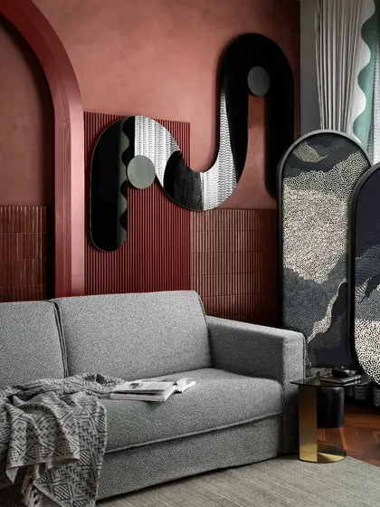 This living space within the guest quarters features a custom-designed, sinuous mirror that acts as a piece of wall art. Paired with an embroidered screen and a comfortable grey sofa, the design is a nuanced interpretation of the client's passion for playful sophistication.