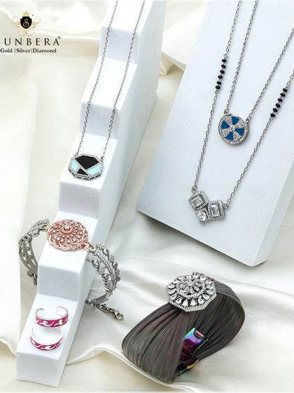 Shimmer with sophistication. This professionally styled shot displays a variety of our silver jewellery pieces on modern white stands. It includes necklaces, bracelets, rings, and a brooch, highlighting the breadth of our design capabilities for everyday fashion.