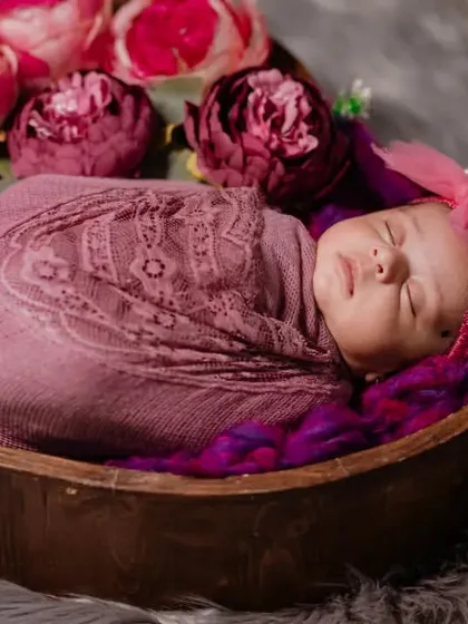 A heart-shaped wooden bowl provides the perfect nest for this sleeping newborn, swaddled in pink and surrounded by matching flowers.