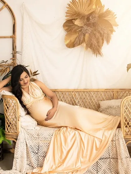 A serene solo portrait in the boho corner. The expecting mother reclines on the wicker sofa, bathed in a warm, sunny light, creating a tranquil and beautiful image.