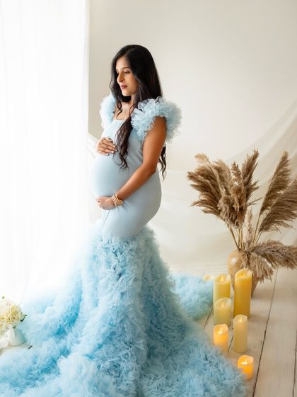 This portrait captures the mom-to-be looking thoughtfully out a window, her hand resting on her bump. The dramatic trail of the blue gown and the soft candlelight create a truly stunning image.