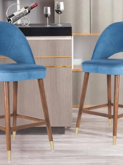 These wooden bar stools feature a comfortable, upholstered seat in blue fabric and gold-tipped legs. They are perfect for adding a pop of color to a kitchen counter or bar.