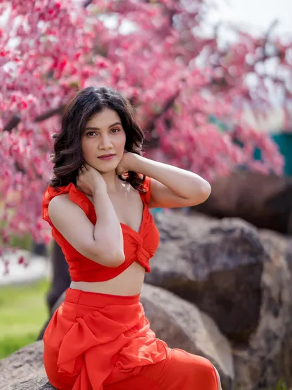 A close-up portrait of the model in the red co-ord set, framed by beautiful pink blossoms.