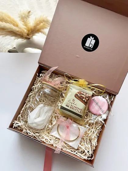 The inside of a bridesmaid proposal box, featuring a personalized bracelet, almond brittle, and other small, thoughtful items.