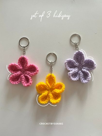 A set of three hibiscus flower keychains in bright pink, yellow, and lilac. These tropical-inspired charms are perfect for adding a summery vibe to your accessories.