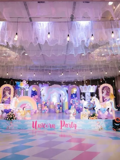This is the kind of magic we love to create. For this unicorn-themed birthday party, we transformed a huge hall with a custom-built stage, pastel rainbow decor, and a dreamy ceiling treatment with draped fabric and hanging lights.
