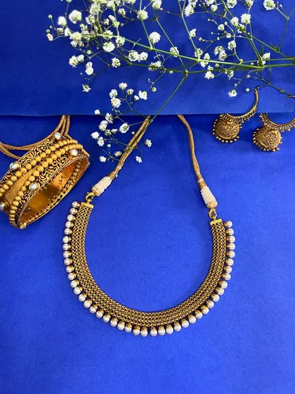 Shine like never before with this golden ensemble. A pearl-lined neckpiece, matching jhumka earrings, and a statement kadda bangle that blend tradition and elegance perfectly.