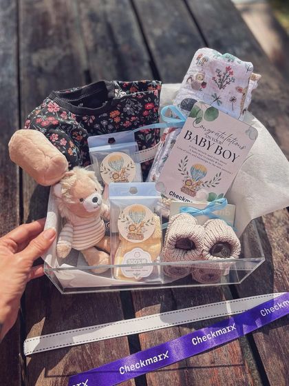 For new beginnings. This clear hamper for a baby boy is filled with soft essentials like a swaddle, booties, and a plush toy, all curated with a gentle and loving touch for a corporate client.