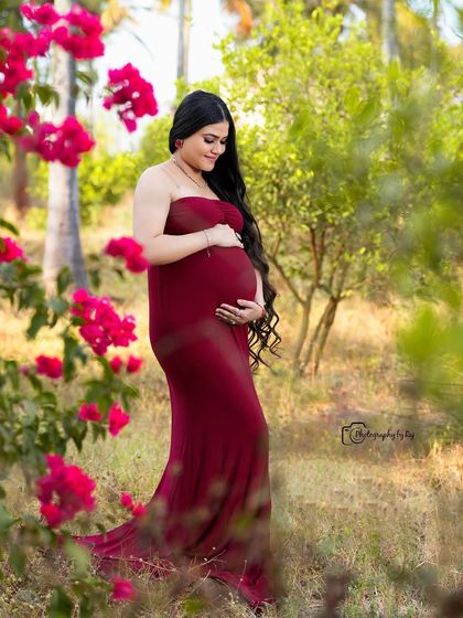 A beautiful solo portrait in a garden of flowers. The mother-to-be wears a simple, elegant red fabric wrap that highlights her baby bump perfectly.