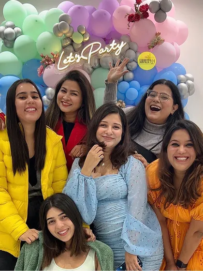Our team and friends celebrating in front of a "Let's Party" neon sign and a colorful pastel balloon backdrop. We love what we do, and we love celebrating with our community.