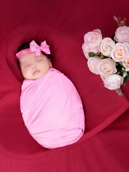 Swaddling is a key part of my newborn sessions, as it keeps babies feeling secure and content. Here, a baby girl is wrapped in a soft pink swaddle, complemented by a bouquet of roses.