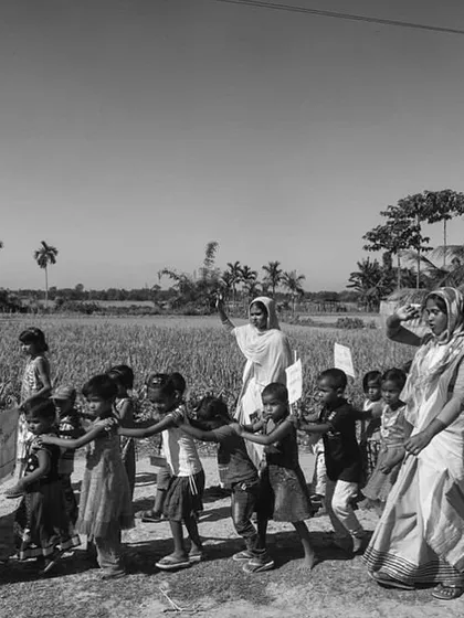 A line of children led by women through a rural landscape in Assam. This photograph documents the community efforts and the role of healthcare workers in managing child nutrition.