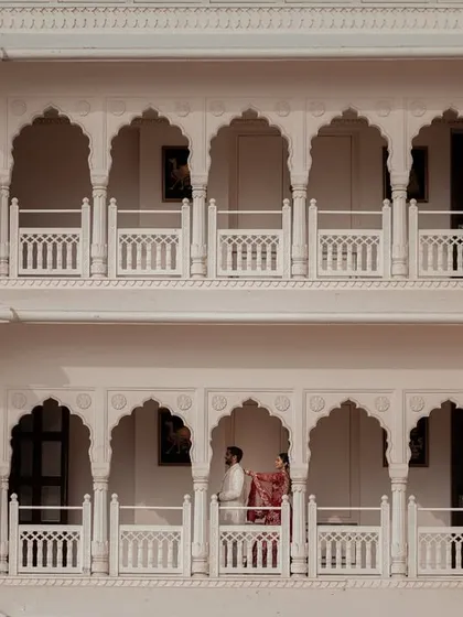 The palace architecture frames the couple on a balcony, creating a sense of timeless romance and quiet intimacy amidst the grandeur. This shot showcases our eye for creative composition in royal wedding photography.