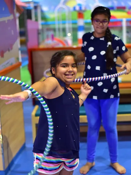 A girl smiles as she masters the hula hoop. My camps encourage kids to try new things and build confidence, with instructors on hand to guide and cheer them on.
