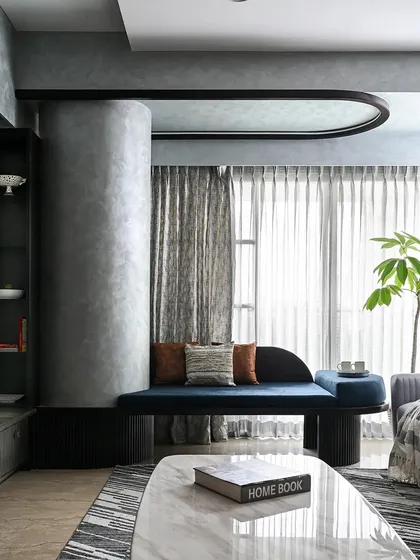 We believe architectural challenges are design opportunities. This custom-designed curved seating, finished in a bold blue fabric, elegantly wraps around a structural column, transforming it from an obstruction into a stunning and functional focal point in the living room.