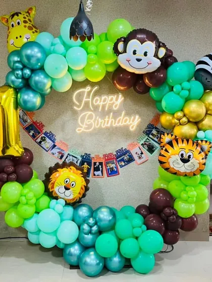 A circular balloon frame for a jungle themed birthday. The ring is decorated with green balloons, animal foil balloons, and a photo banner of the birthday child's first year.