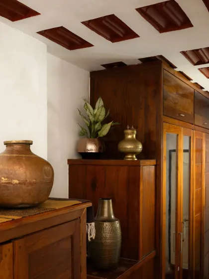 A detail shot showcasing the home's timeless tribute to heritage. Antique brass and copper vessels are displayed against rich, dark wood cabinetry and a traditional waffle slab ceiling.