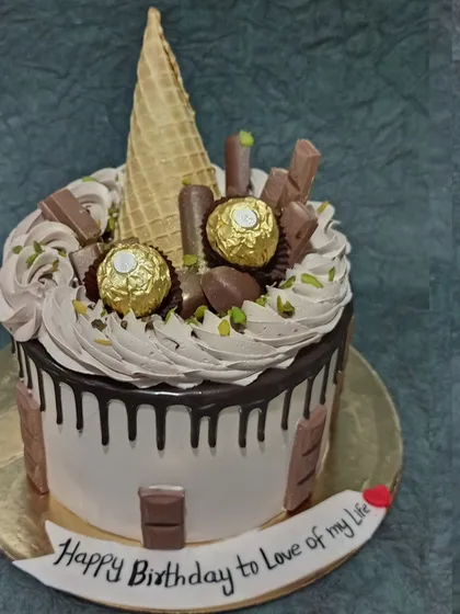 A decadent chocolate overload cake. This drip cake is topped with Ferrero Rocher, KitKats, and an ice cream cone, perfect for any chocolate lover.