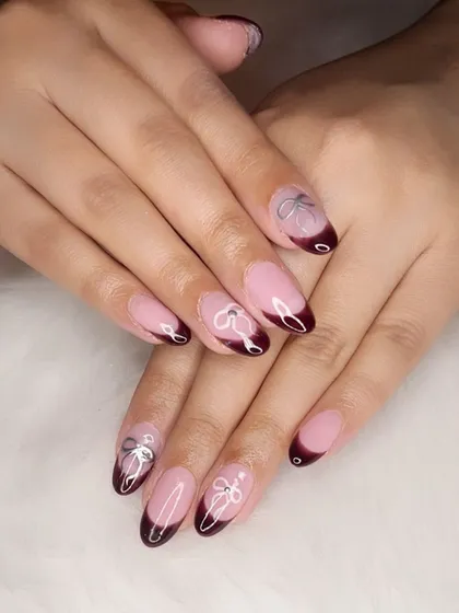 Coquette-style French manicure with deep cherry-chocolate tips and delicate hand-painted silver bows.