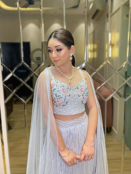 A client ready for a party in a stylish grey sharara set. The blouse features delicate floral embroidery, and the attached cape-like sleeves add a modern flair.