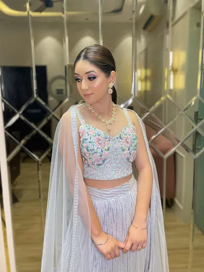 A client ready for a party in a stylish grey sharara set. The blouse features delicate floral embroidery, and the attached cape-like sleeves add a modern flair.