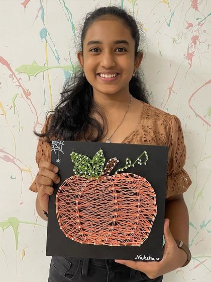 A spooky and fun Halloween creation. This young artist proudly shows off the pumpkin string art she made at our seasonal workshop.