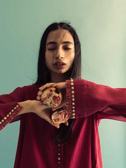A conceptual portrait for Swatti Kapoor. The model holds a broken pomegranate, with the rich red of the fruit echoing the color of her dress.