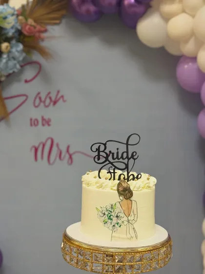 The cake is always a centerpiece. This elegant "Bride to be" cake features a hand-painted design and is placed on a crystal stand, complementing the purple and blue party decor.