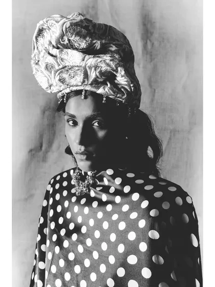 A close-up black and white portrait from the same series. The lighting carves out the model's features and highlights the texture of the turban-style headwrap.