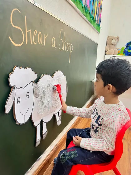 With careful strokes, a child helps give our cardboard sheep a haircut. This activity is part of our thematic learning approach, making education an interactive adventure.