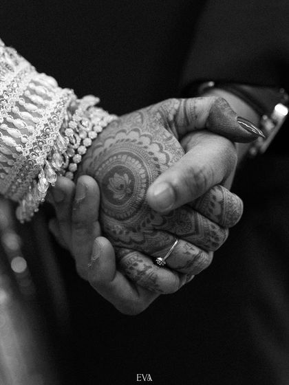 A black and white close-up of the couple holding hands, showcasing the bride's henna and the simple elegance of the moment.