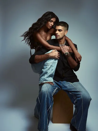 This color portrait from the 'Love/25' series showcases a playful and intimate pose. The warm lighting and casual styling create a relatable yet fashionable image, highlighting the couple's chemistry and accessories like the watch and chain necklace.