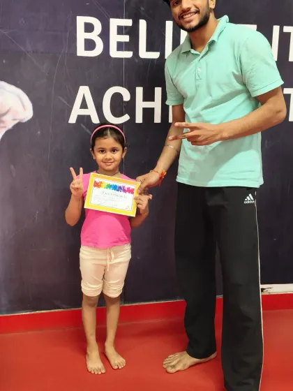 We love celebrating progress. Here, a proud student receives her certificate of achievement from her coach, a special moment that recognizes her hard work and dedication in our kids' fitness program.